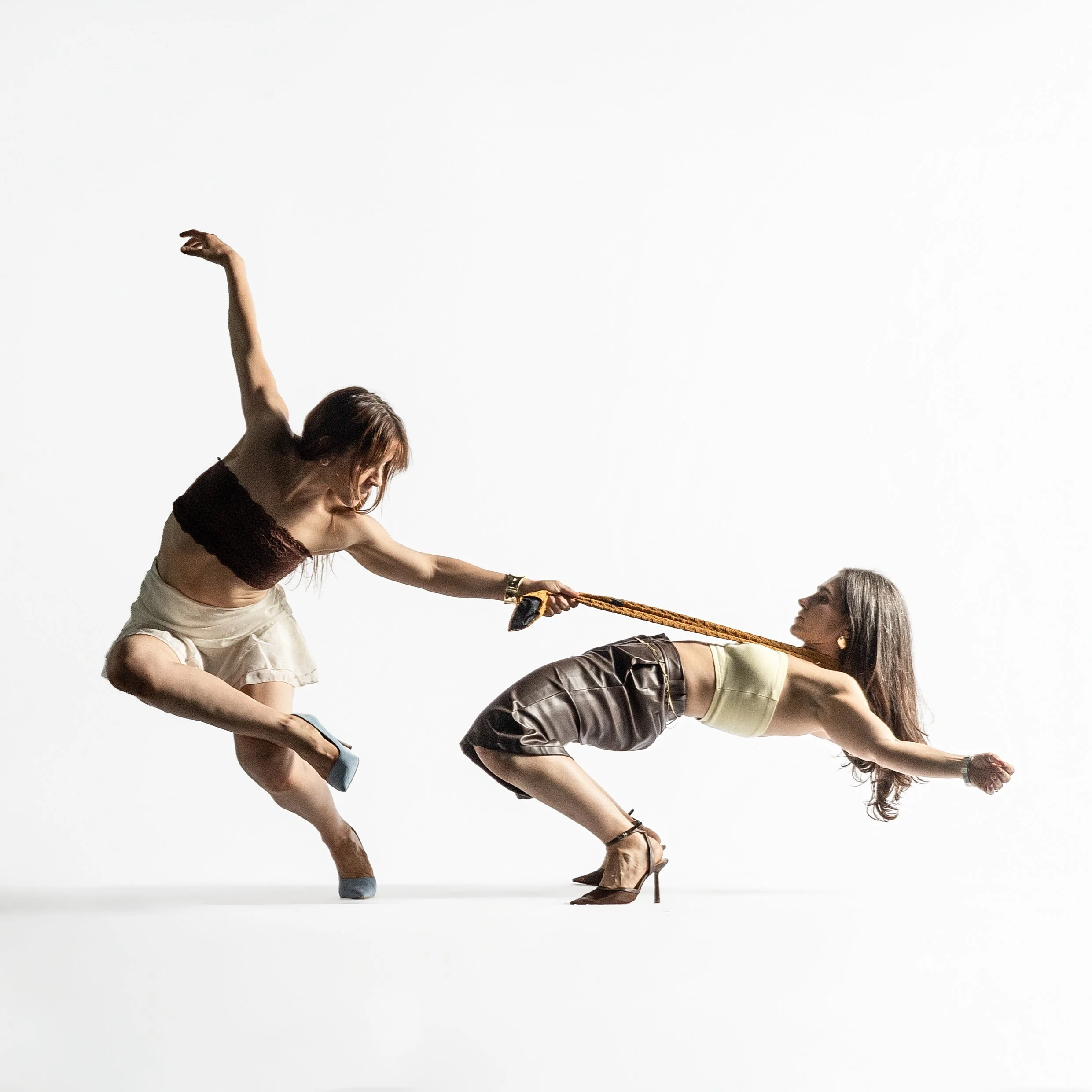 Two women with long hair in stylish outfits, facing each other and holding a rope