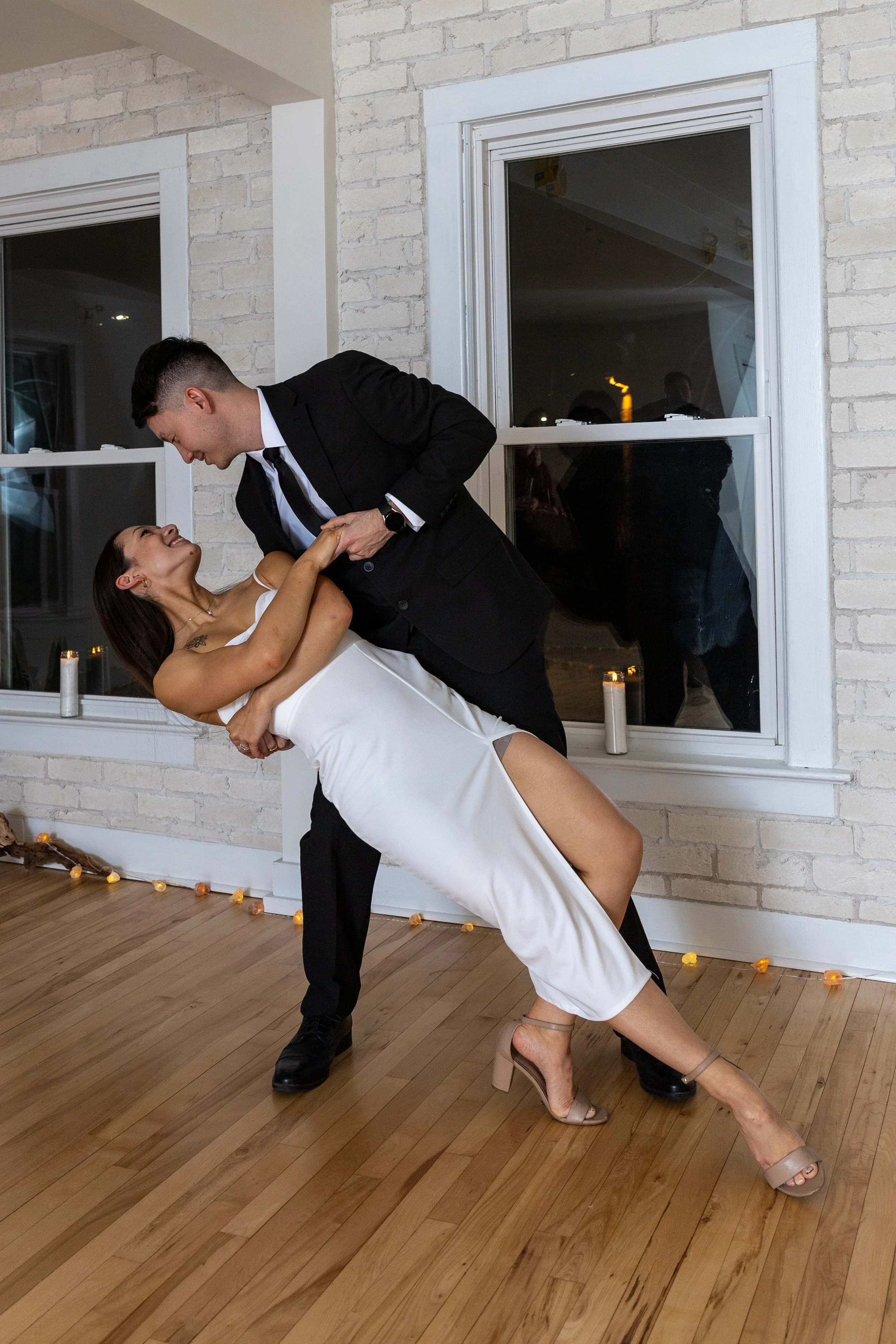 A couple dancing closely at an indoor event, with candles and string lights visible in the background.