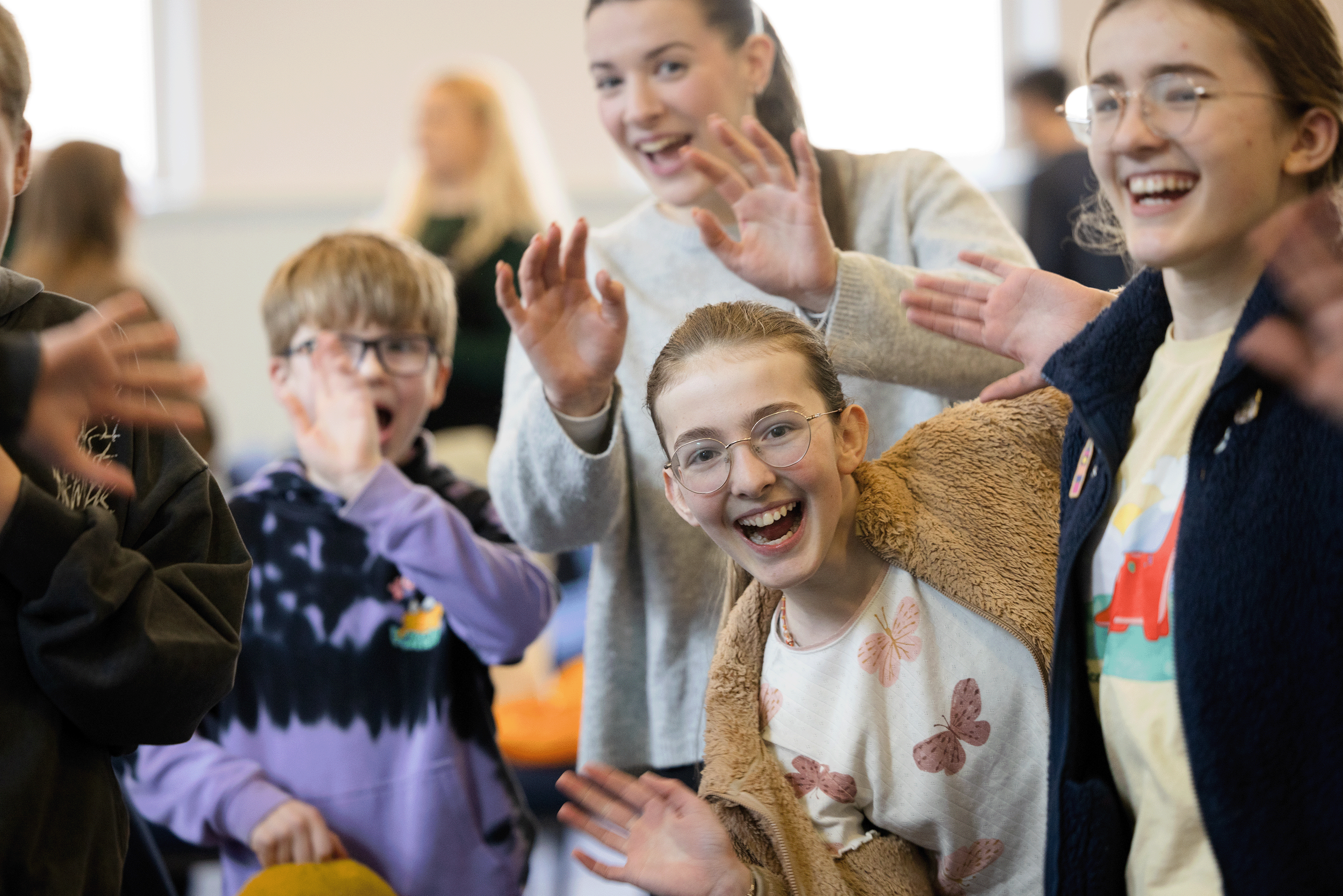 A group of young people together, smiling in a colourful room. A football is held out of focus in the foreground