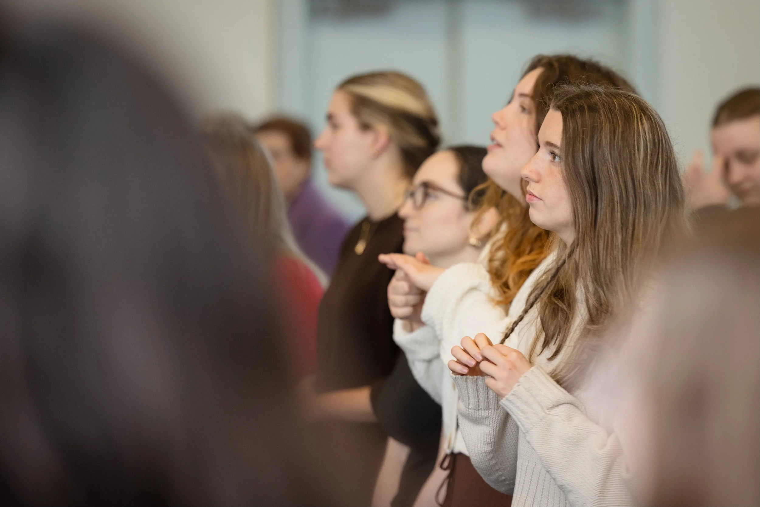 A group of women standing in a line, looking forward, with some holding their hands in front of them, at a church gathering.