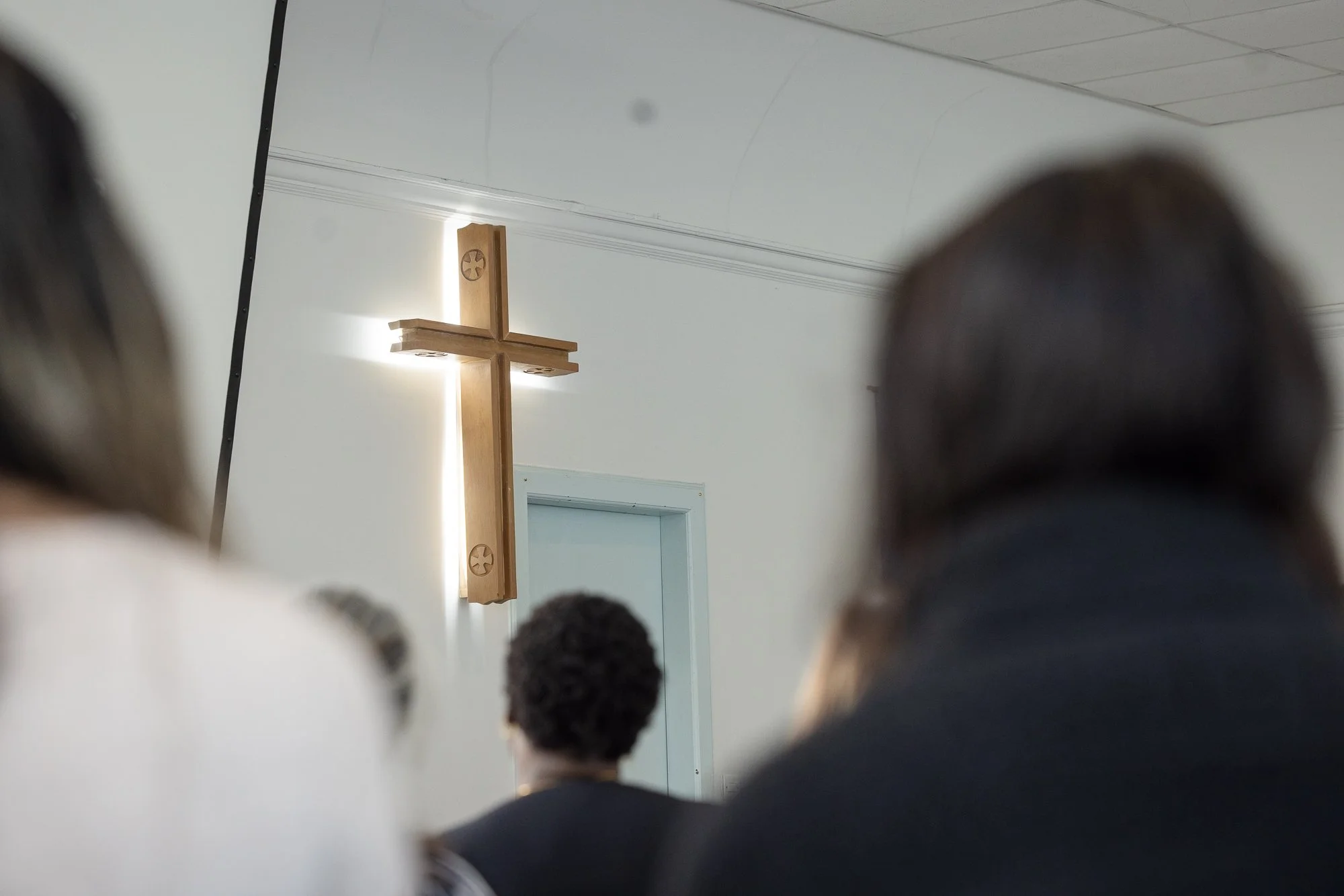 A wooden cross on the wall, a group of people, viewed from behind, looking towards it