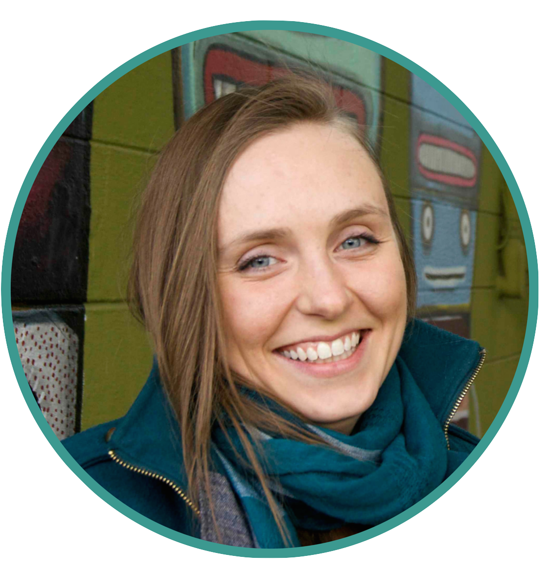 M, a white person with blue eyes and light brown hair, smiles in a jacket and scarf in front of a colorful mural.