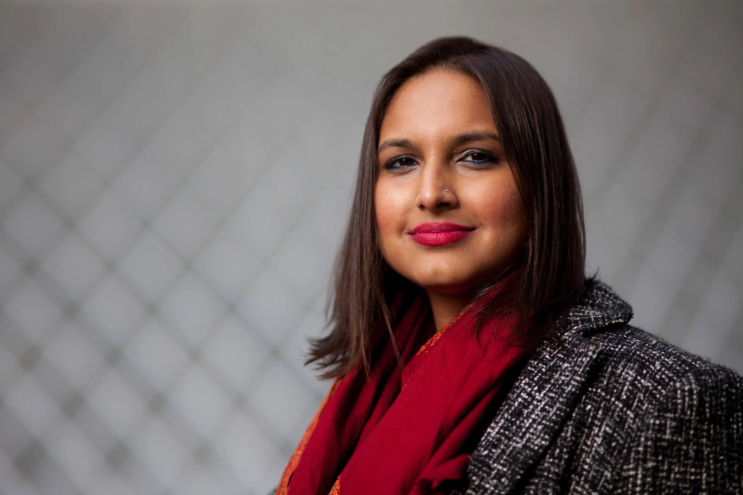 Ruchika T. Malhotra smiles slightly, with shoulder-length straight brown hair, a red scarf, and a jacket.