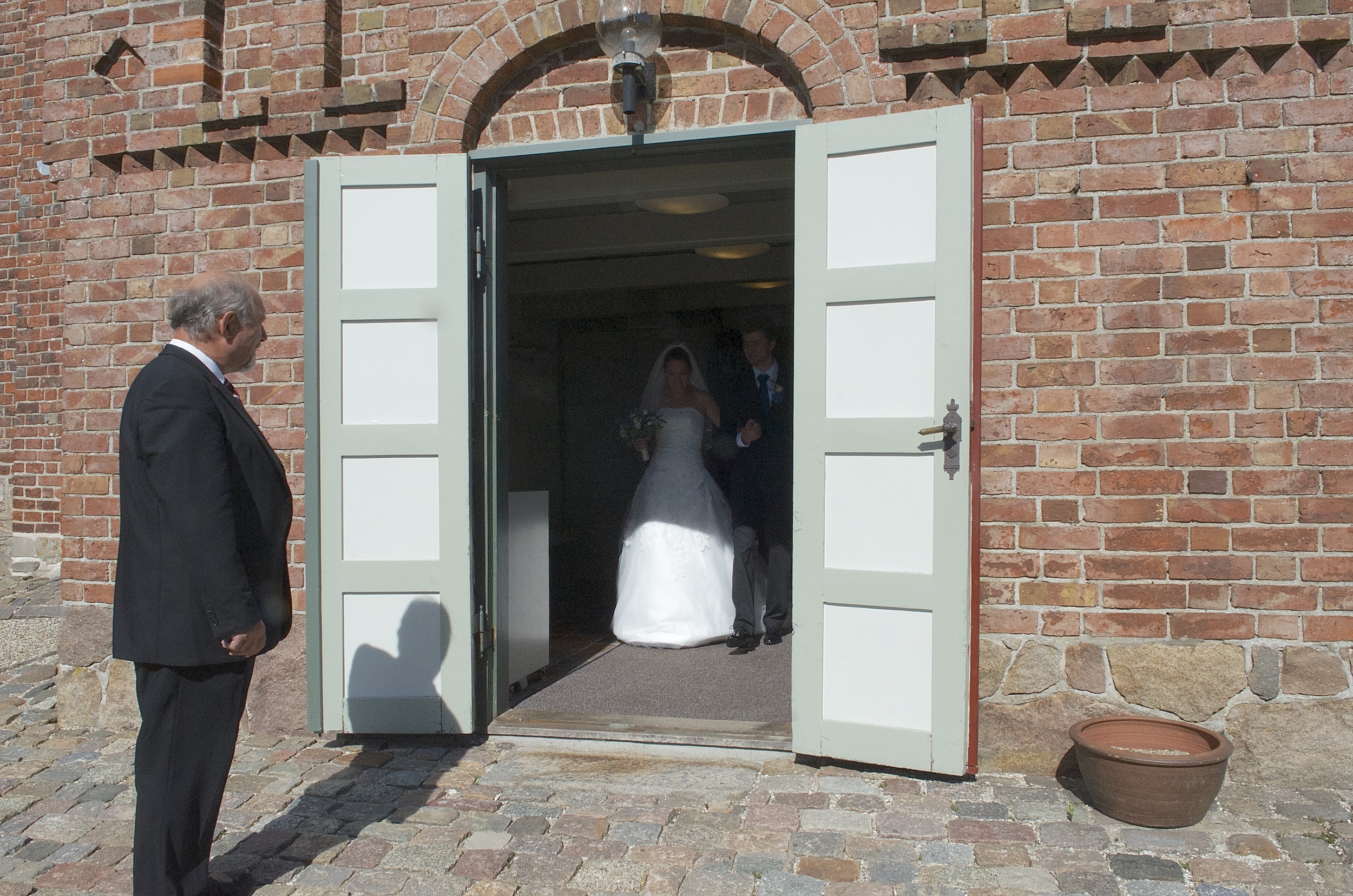 Kuhrt O. Hansen har haft mange hverv ved Blovstrød Kirke. Her tager han som kirketjener imod et netop viet brudepar ved kirkeporten. Det var på datoen 7-9-13. Foto: AOB