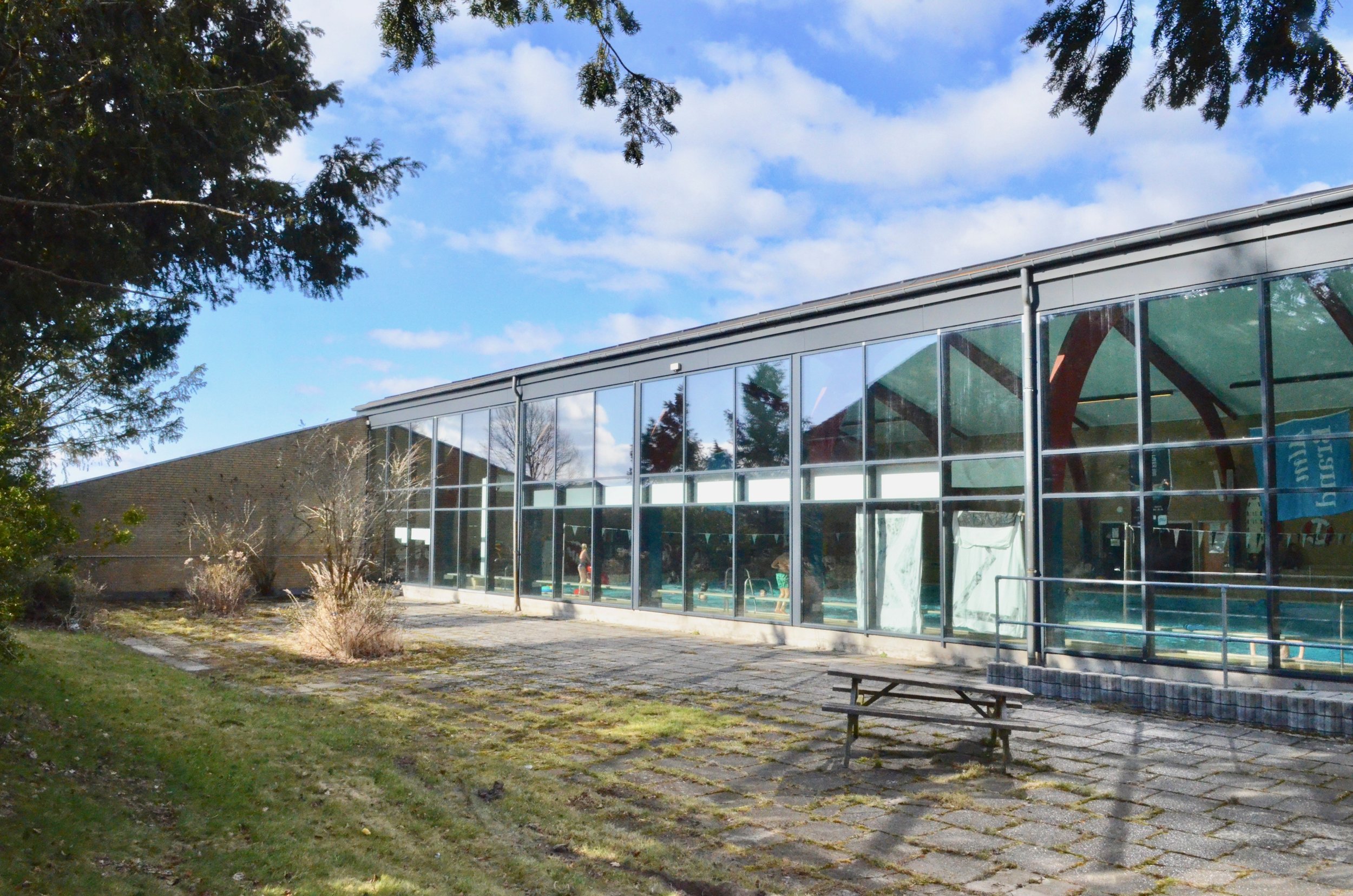 Dryland-tilbygningen etableres langs hele svømmehallens sydfacade mellem de to markante læmure. Det kan ikke undgås, at tilbygningen vil tage en stor del af dagslyset til selve svømmehallen - helt afhængig af, hvor høj tilbygningen bliver. Foto: AOB
