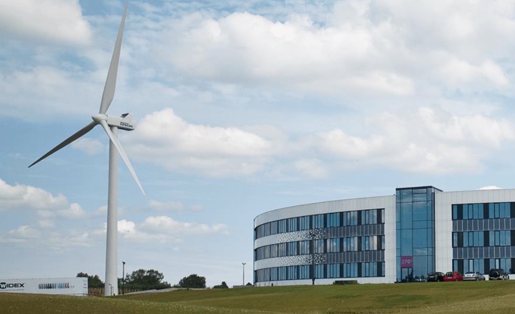 Udover sin runde udformning er Widex' hovedkontor kendt for sin vindmølle, der rejser sig op bag bygningen. Og på bygningens sydfacade er der indlagt solceller. Foto: Widex