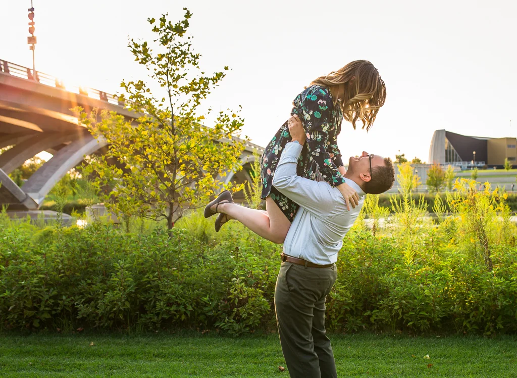 Guy lifts girl off the ground with beautiful greenery and sunset in the background at this Scioto Mile enagagement session.