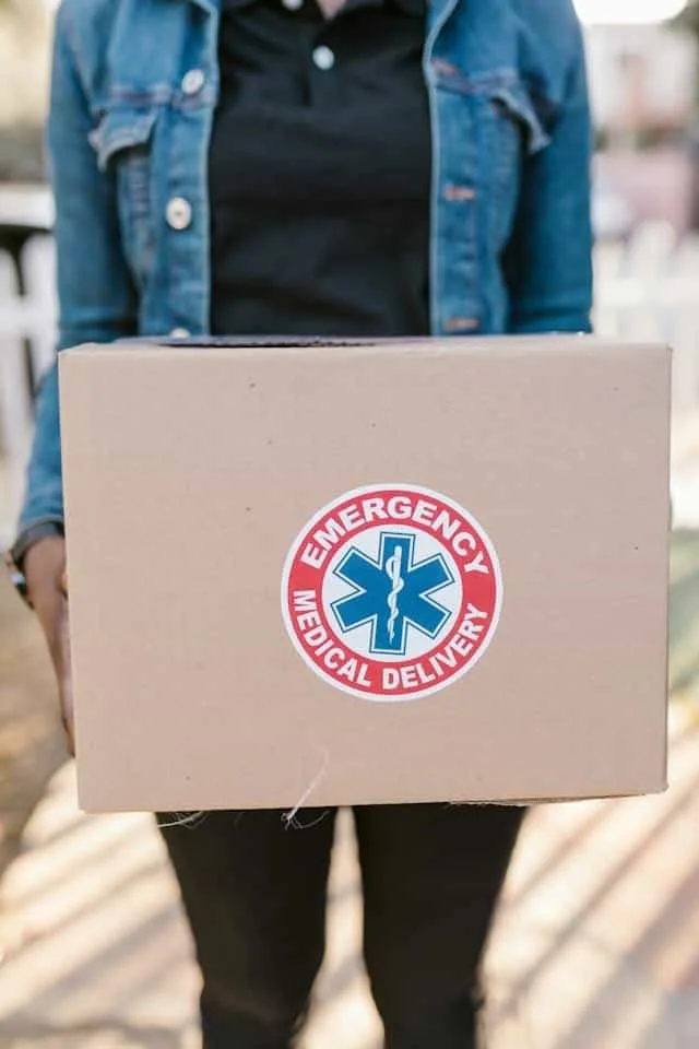 A person holding a cardboard box with an 'Emergency Medical Delivery' sticker.
