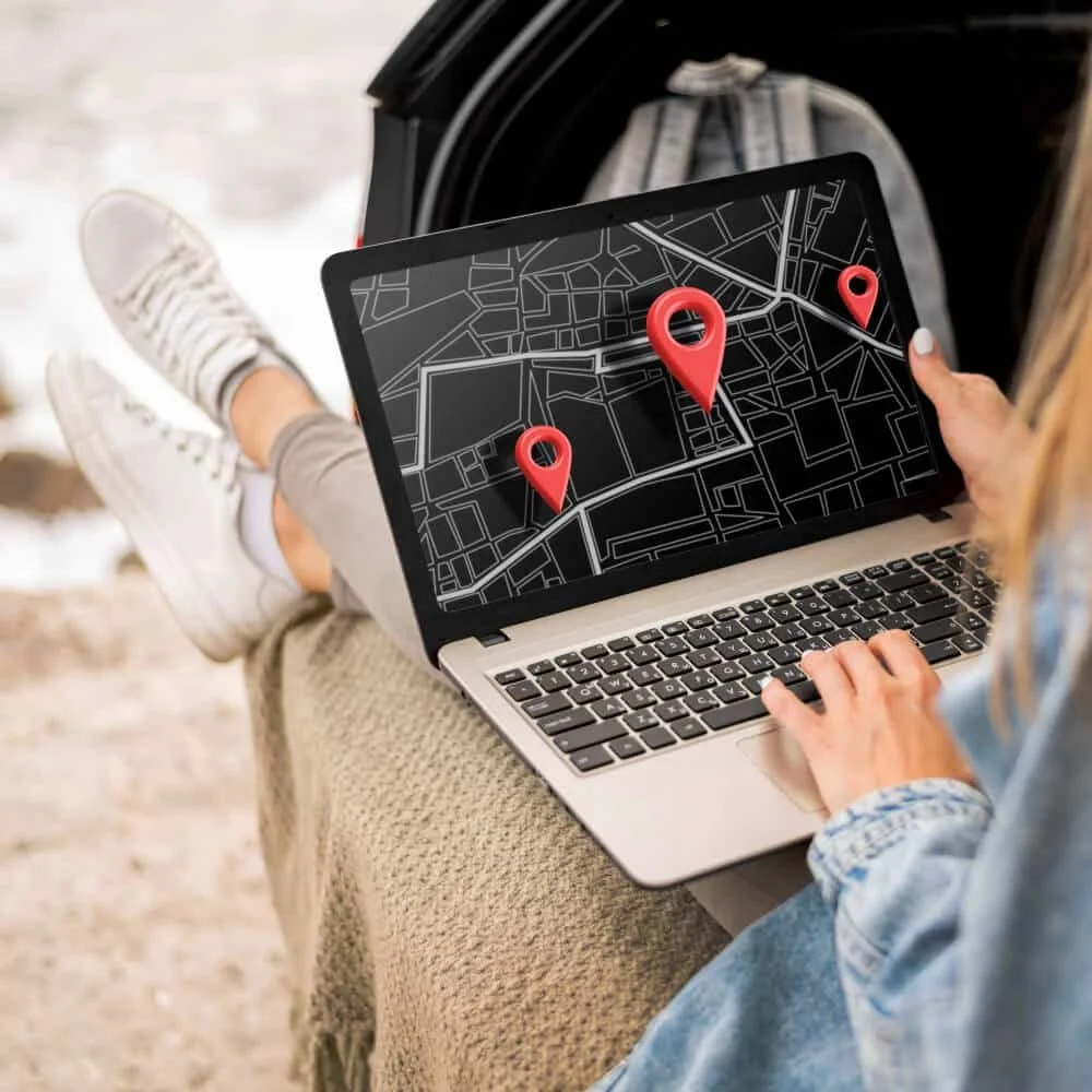Person sitting outdoors with legs up, using a laptop to view a map with three location pins on the screen.