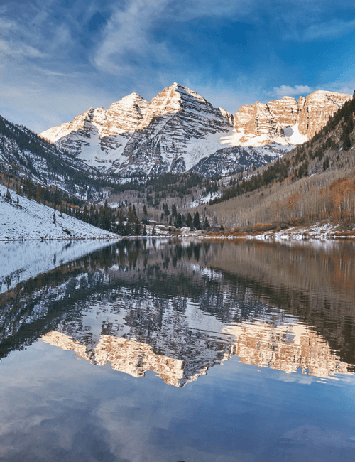 Snow-capped mountains reflected in a calm lake with a partly cloudy sky.