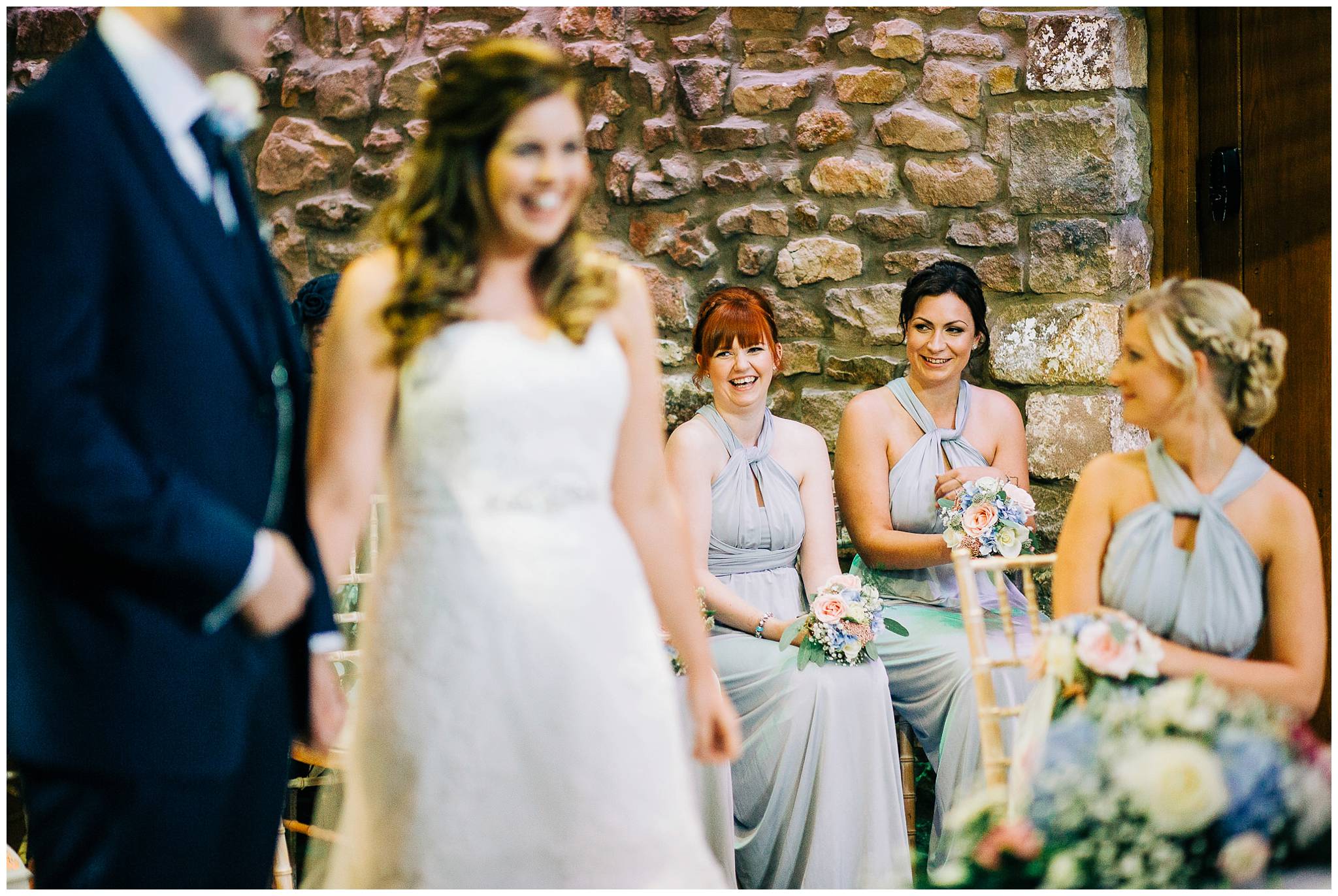 bridesmaids smiling at each other in the background during a ceremony at browsholme hall tithe barn