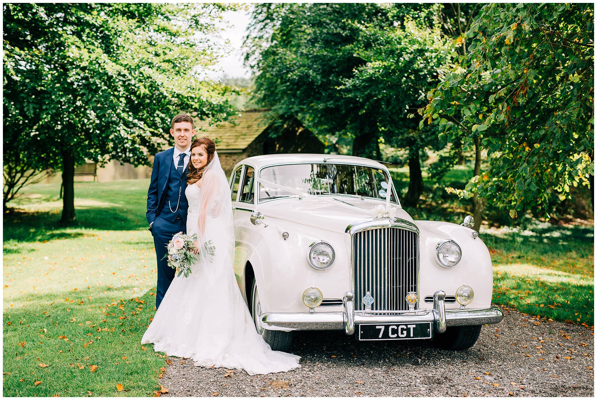 bride and groom stood at the side of vintage bentley with browsholme hall lake in the background