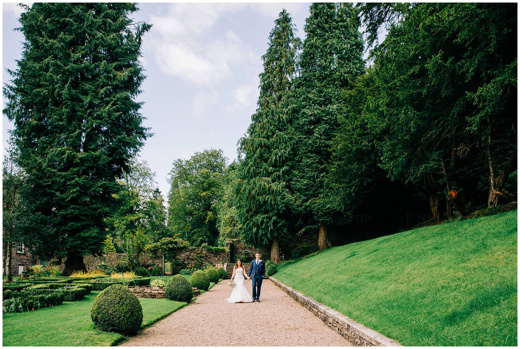 bride and groom walking along pebbled path next to browsholme hall manicured gardens