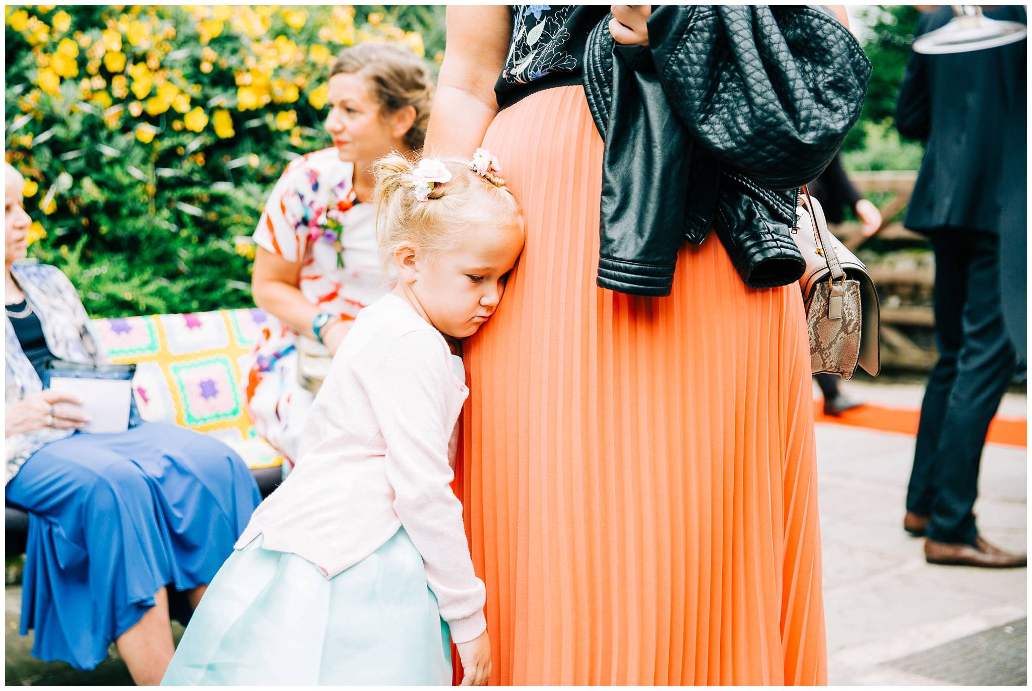 little girl hugging her mothers legs being shy