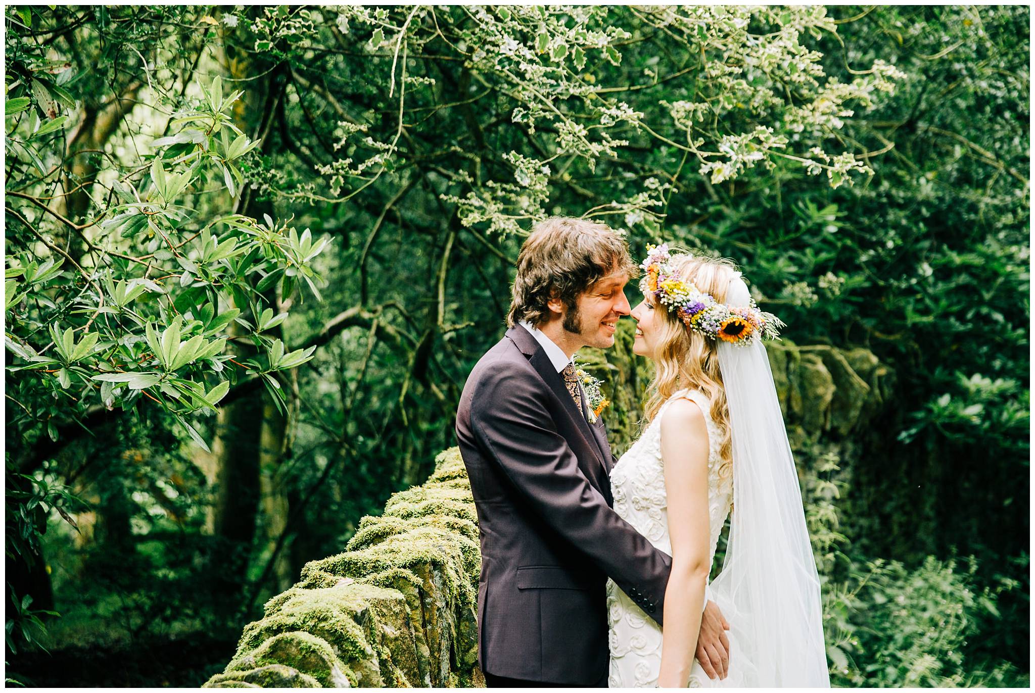 groom leaning against stone wall with his arms around bride