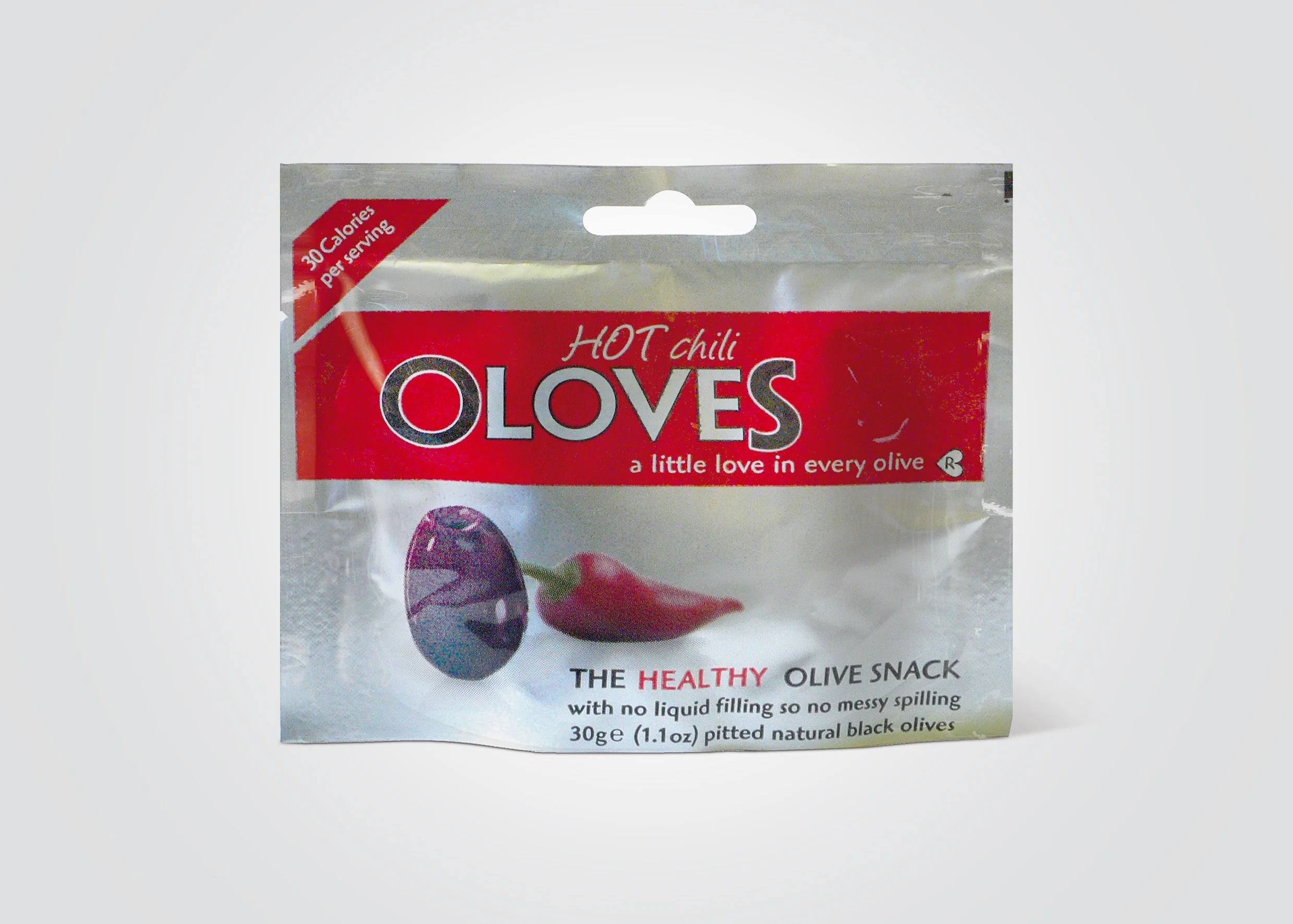 Packaging of a snack called Hot Chili Oloves featuring images of a black olive with a purple tint and a red chili pepper on the front and text highlighting it as a healthy, no liquid filling olive snack with 30 calories per serving.
