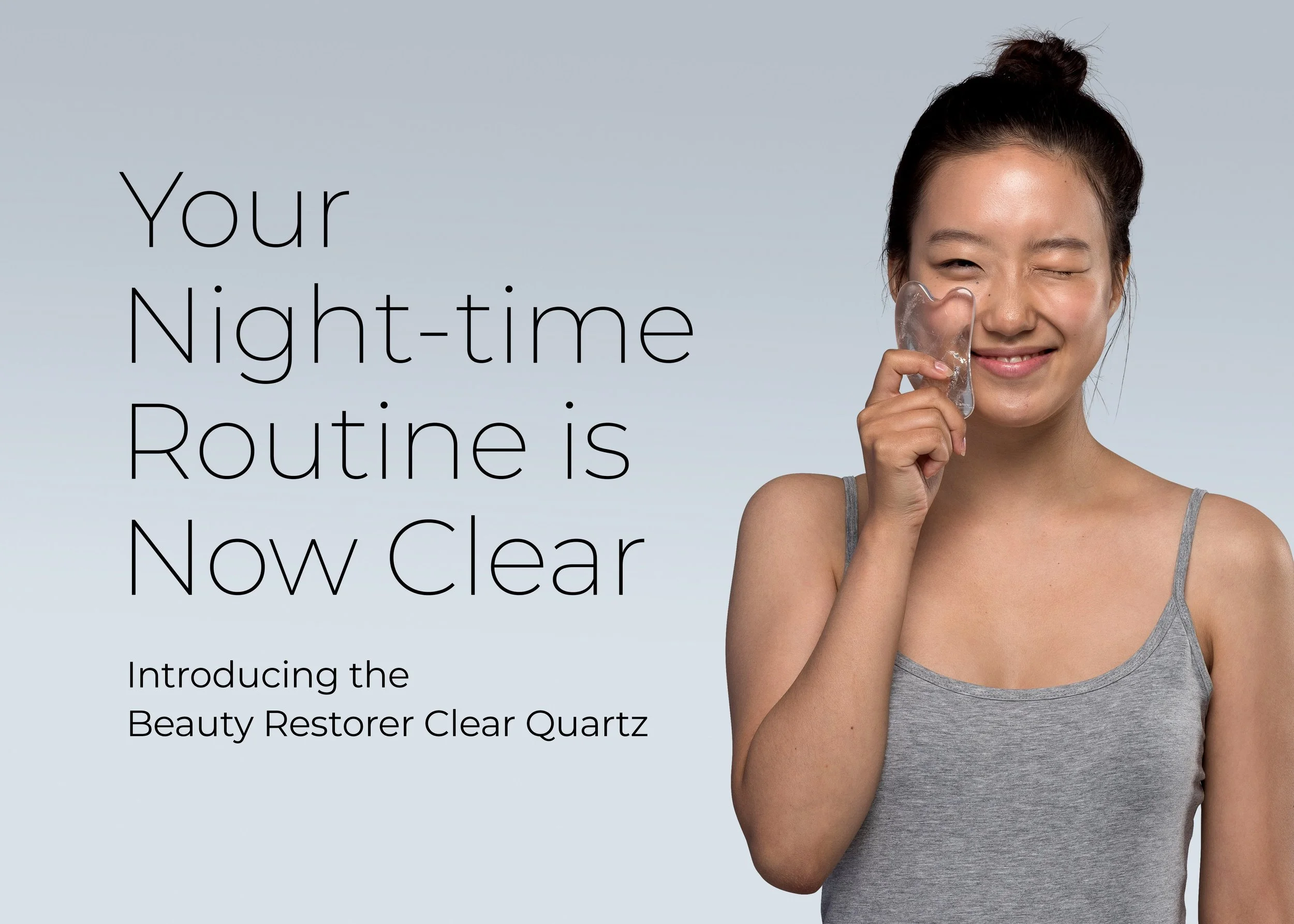 Beautiful woman holding a Hayo'u crystal gua sha tool to her face, smiling and winking. Text on the left side of the image reads 'Your night time routine is now clear. Introducing the Beauty Restorer Clear Quartz.'