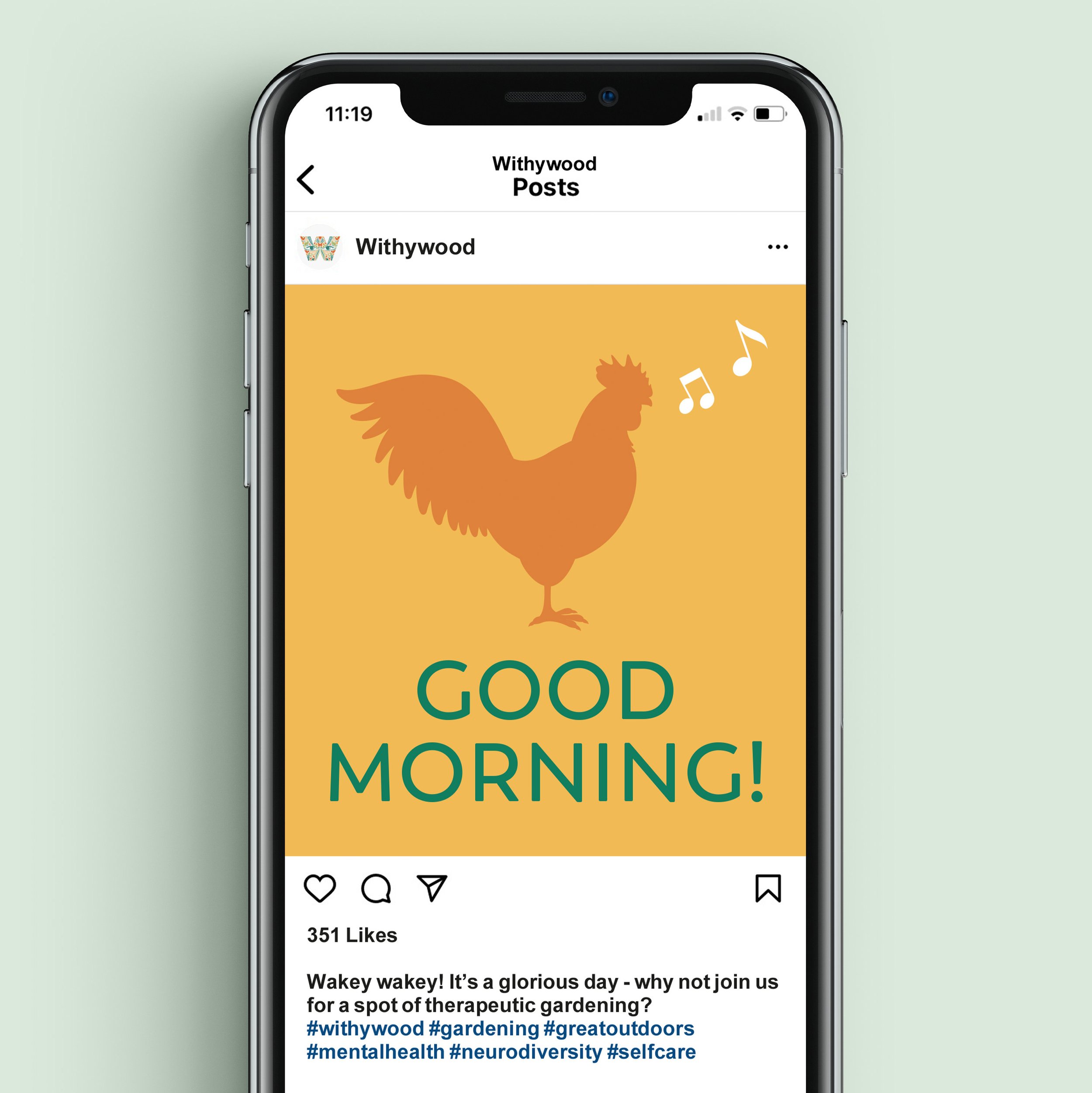 An Apple iphone displaying a Withywood Instagram post with a cockerell crowing Good Morning in brand colours.