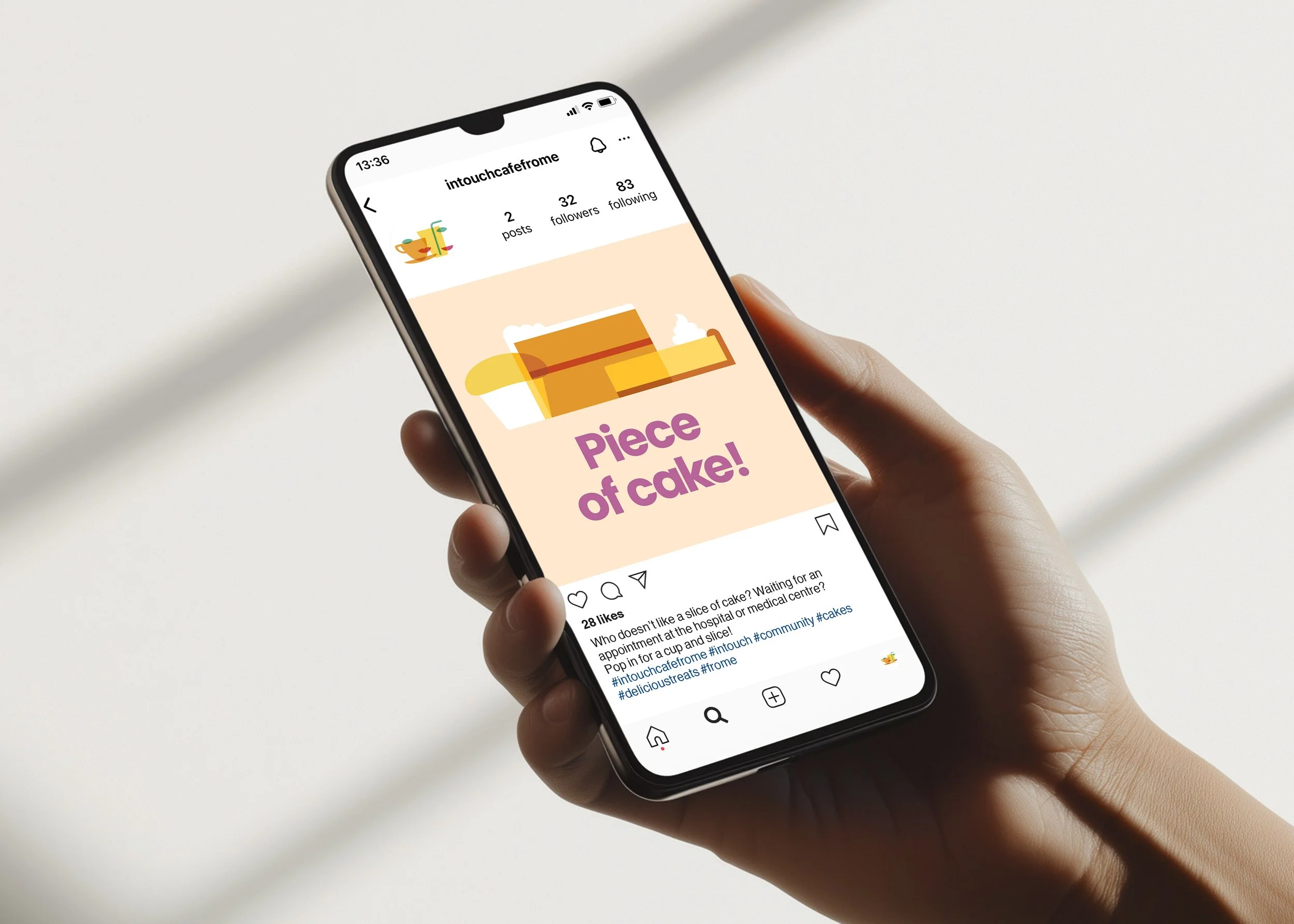 InTouch Café social media post - a hand holding a smartphone displaying an Instagram post with an illustration of a piece of cake and the text 'Piece of cake!'