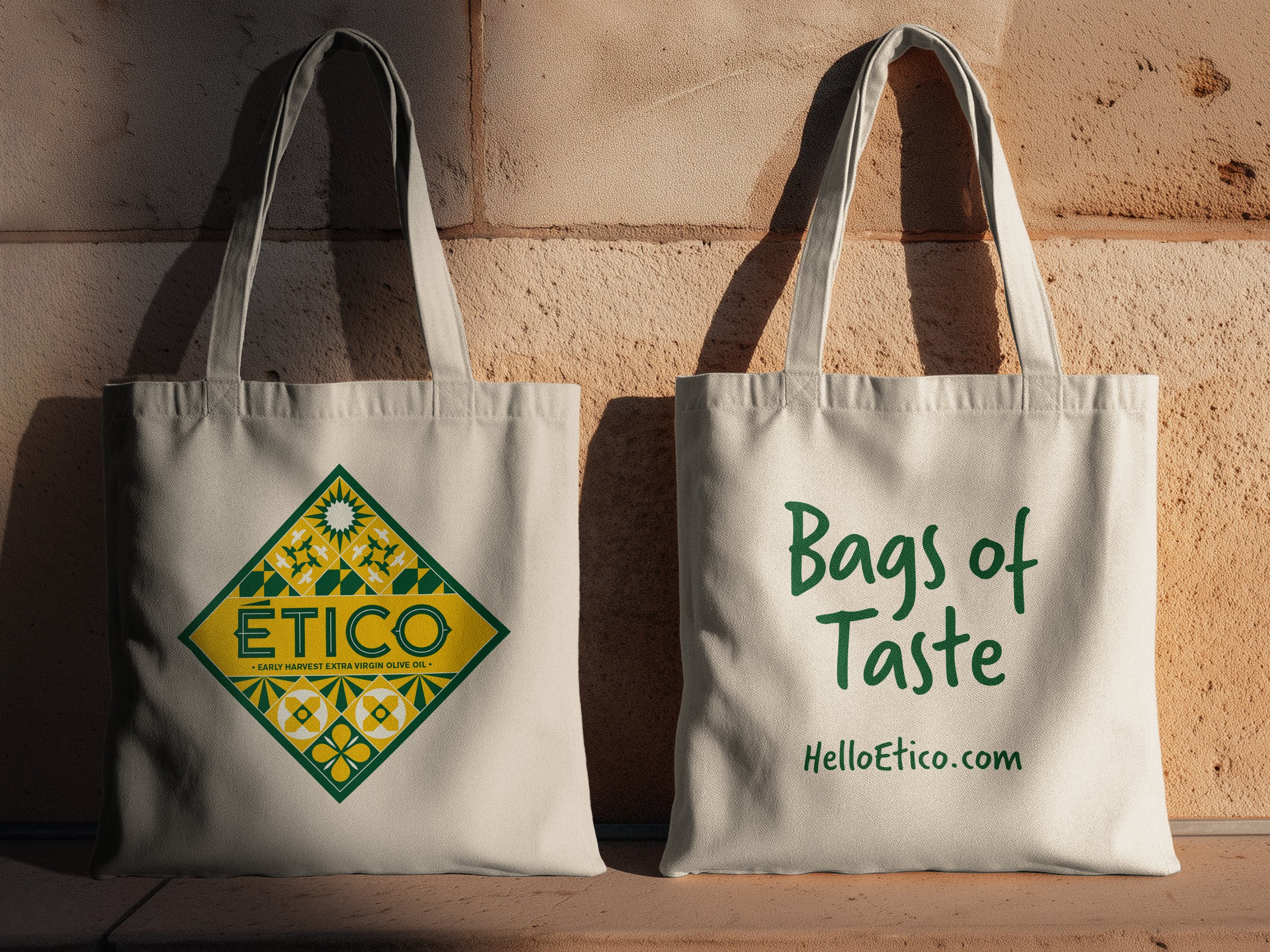 Two sides of an Ético tote bag - one showing the brand diamond with the ético branding and tiles, the other displays the witty copyline "Bags of Taste" and the website address. Both are sat next to a wall in Spain.