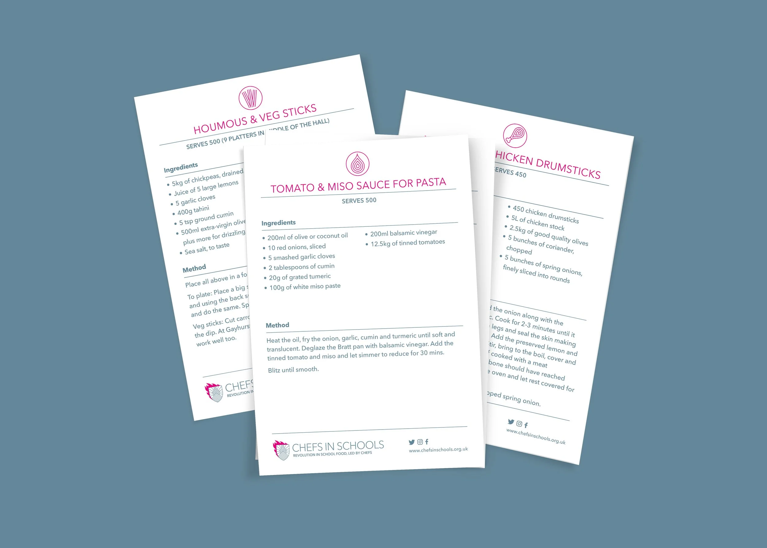 Chefs in Schools - Three recipe printouts with ingredients and instructions for dishes including hummus and veggie sticks, tomato and miso sauce for pasta, and chicken drumsticks, laid out overlapping on a blue surface.