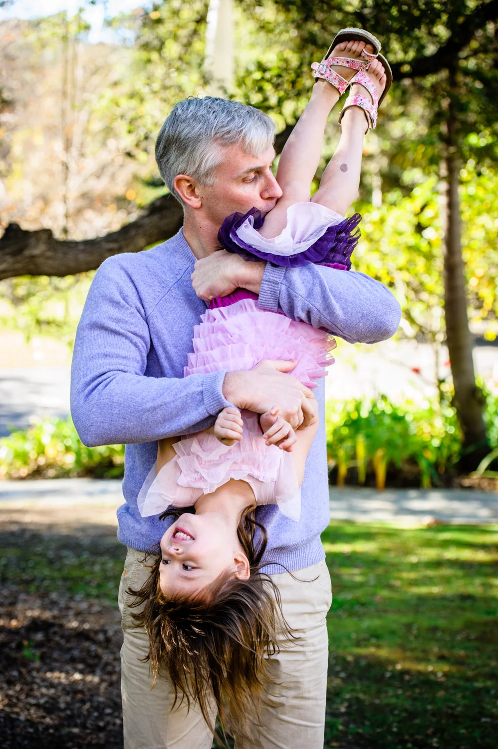 Dad holds smiling daughter upside-down.