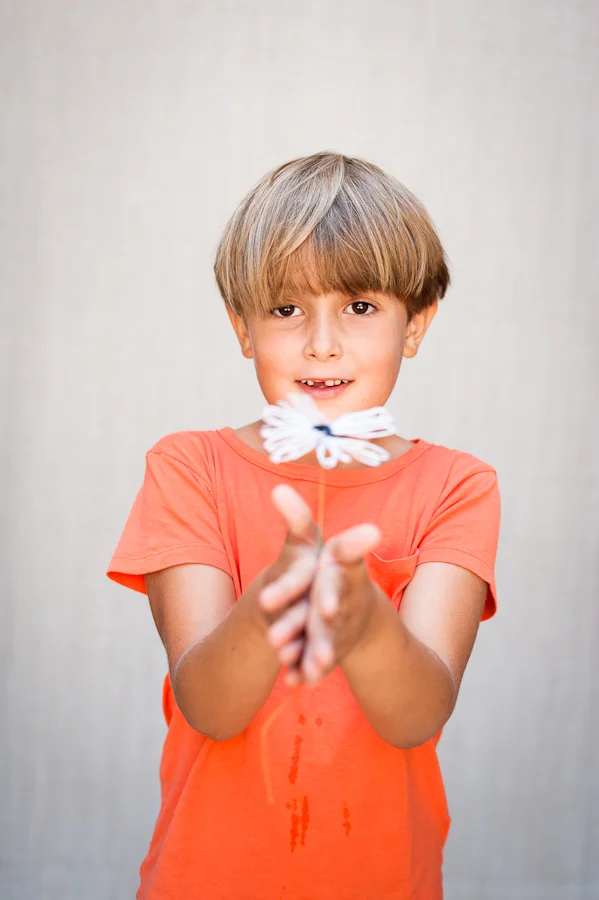Boy in orange shirt holding white flower.