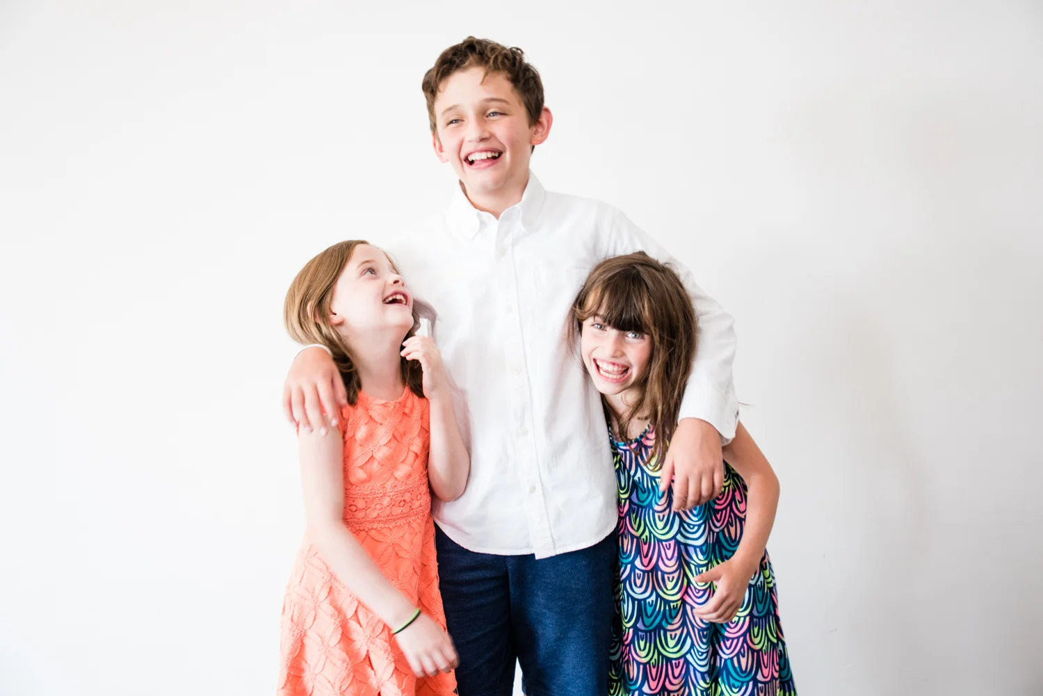 Brother and two sisters against white wall laughing.