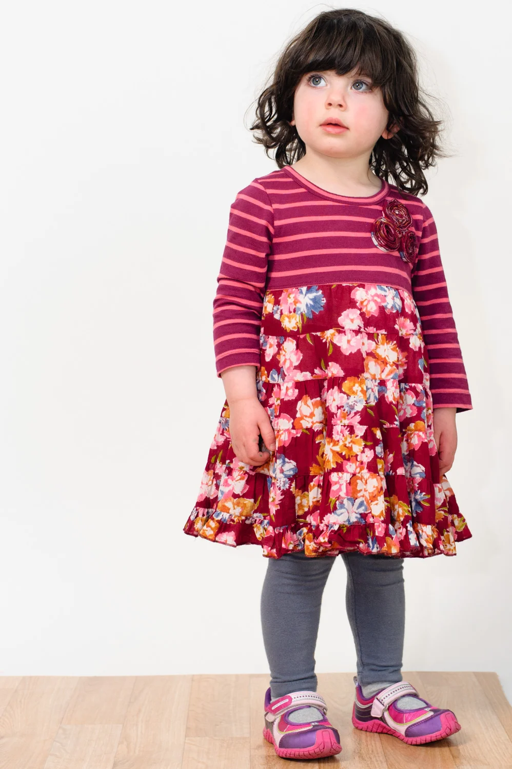 Toddler in patterned dress with tights and pink sneakers.