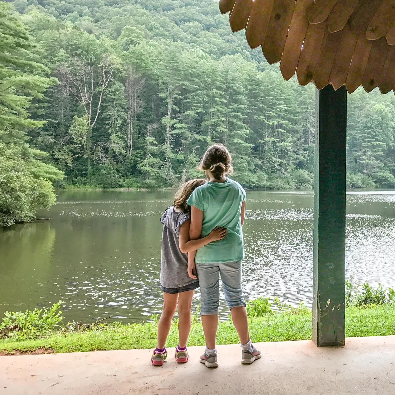Young sisters look out at a lake together.