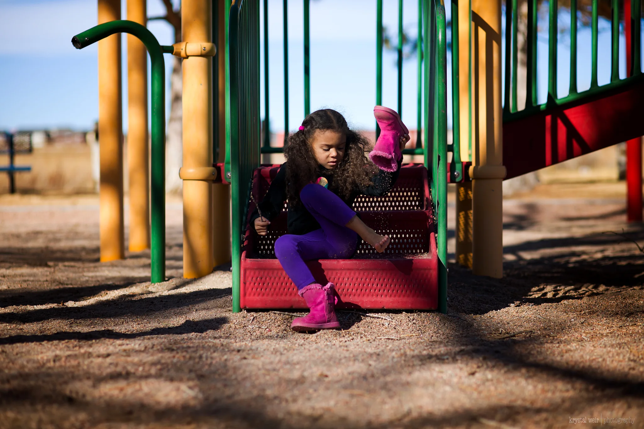 Day 35/365 We always leave the playground with a few bits and pieces in our shoes Another nice day after snow so we headed to the neighborhood playground. A lot of running and hiding, so of course we collected gravel in our shoes and had to empty them out before we left. With this image there are a lot of shadows and colors. Images like this I usually scrap because I used to think dark shadows and harsh sun was not a great look in a photo, but I have come to embrace shooting in harsh daylight. I now see the shadows as a way to add depth and interest to an image. i also decided for this image to make those colors pop because this is a picture of childhood and kids love colorful things. 