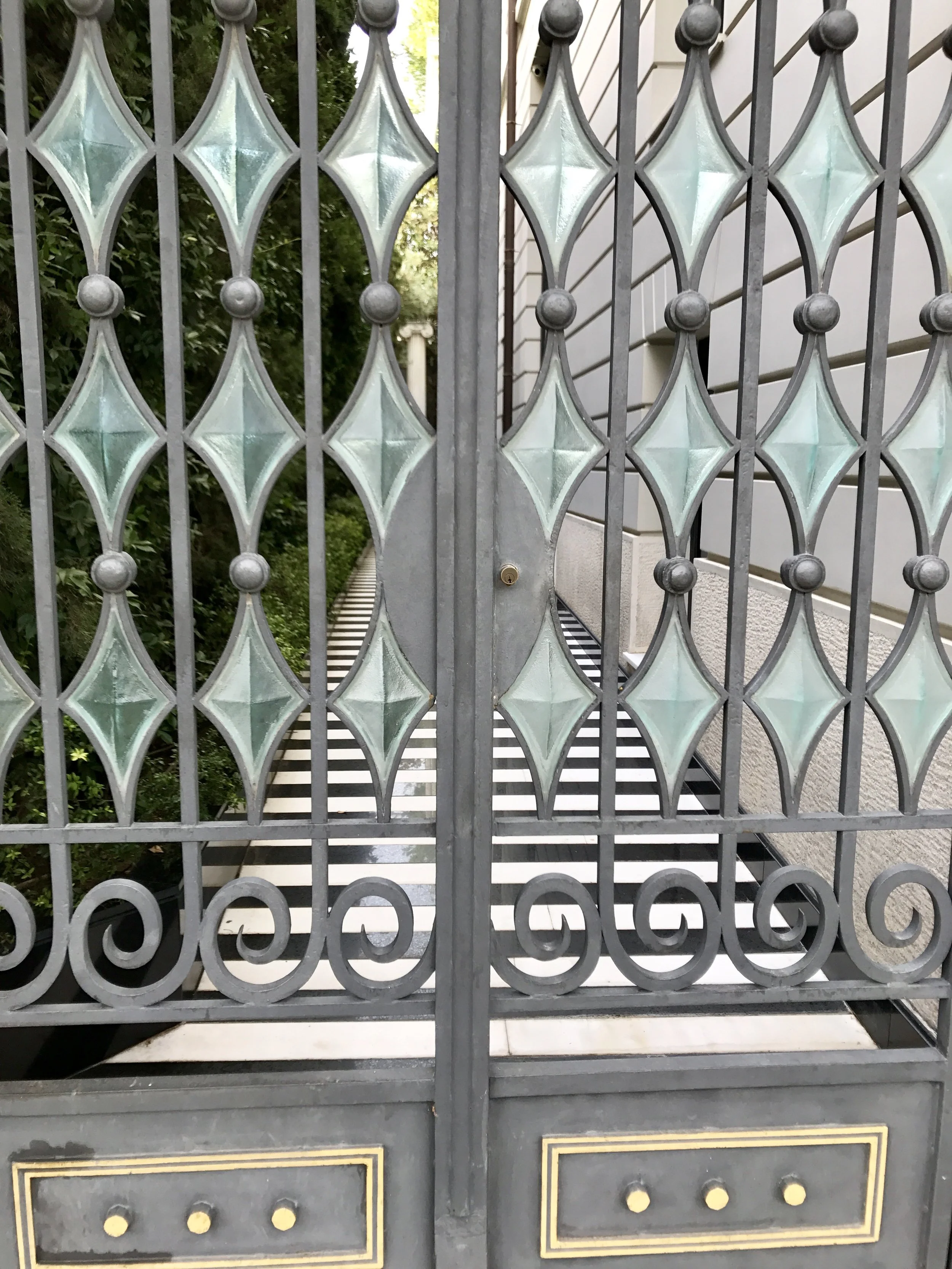 Cast glass set in a decorative and functional gate guarding a black and white striped marble side walk.