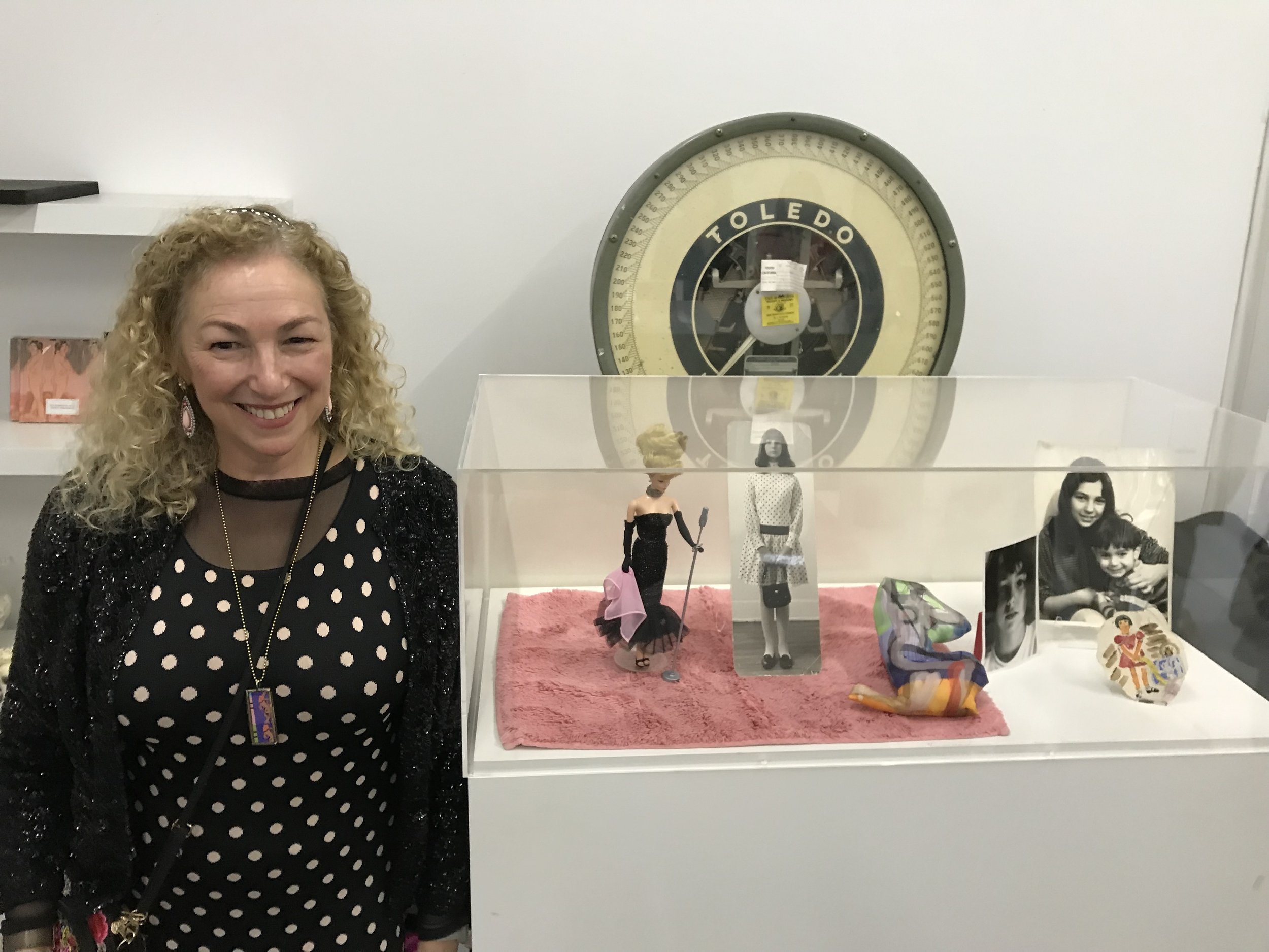 Next to the vitrine which contains old black and white photos of me taken by my father, a tiny old watercolor of mine, a new Barbie (re-issued anniversary edition) like one of my first, my first art doll I made in 2016, and a little pink bath mat that represents the floor.
