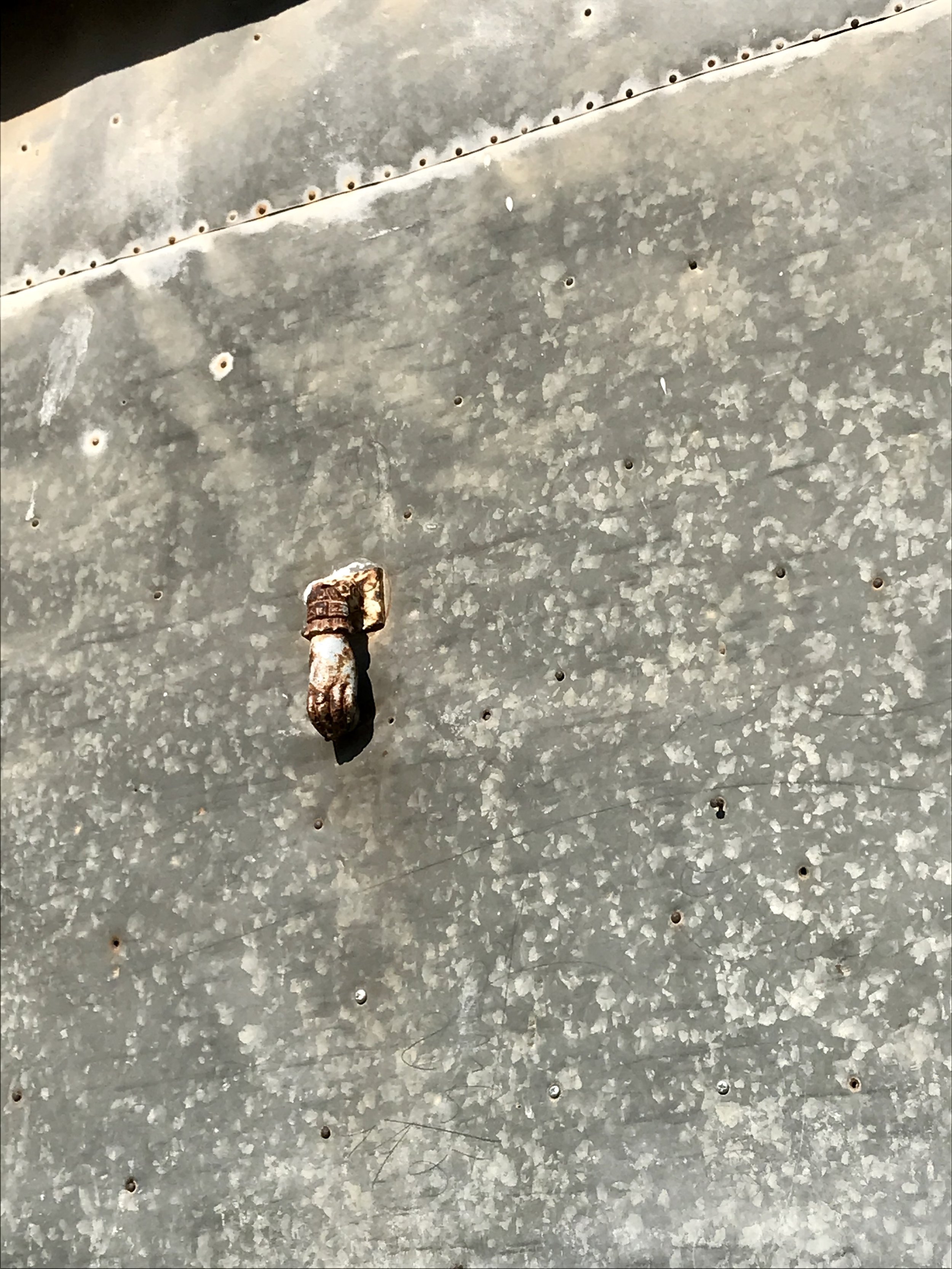 Tiny delicate hand knocker on big, plain metal door