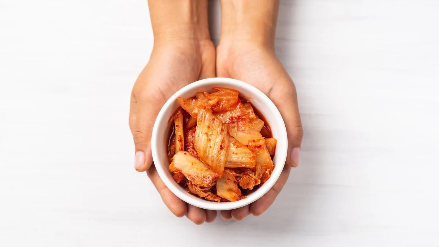 someone holding a small white bowl in their hands with kimchi in the bowl