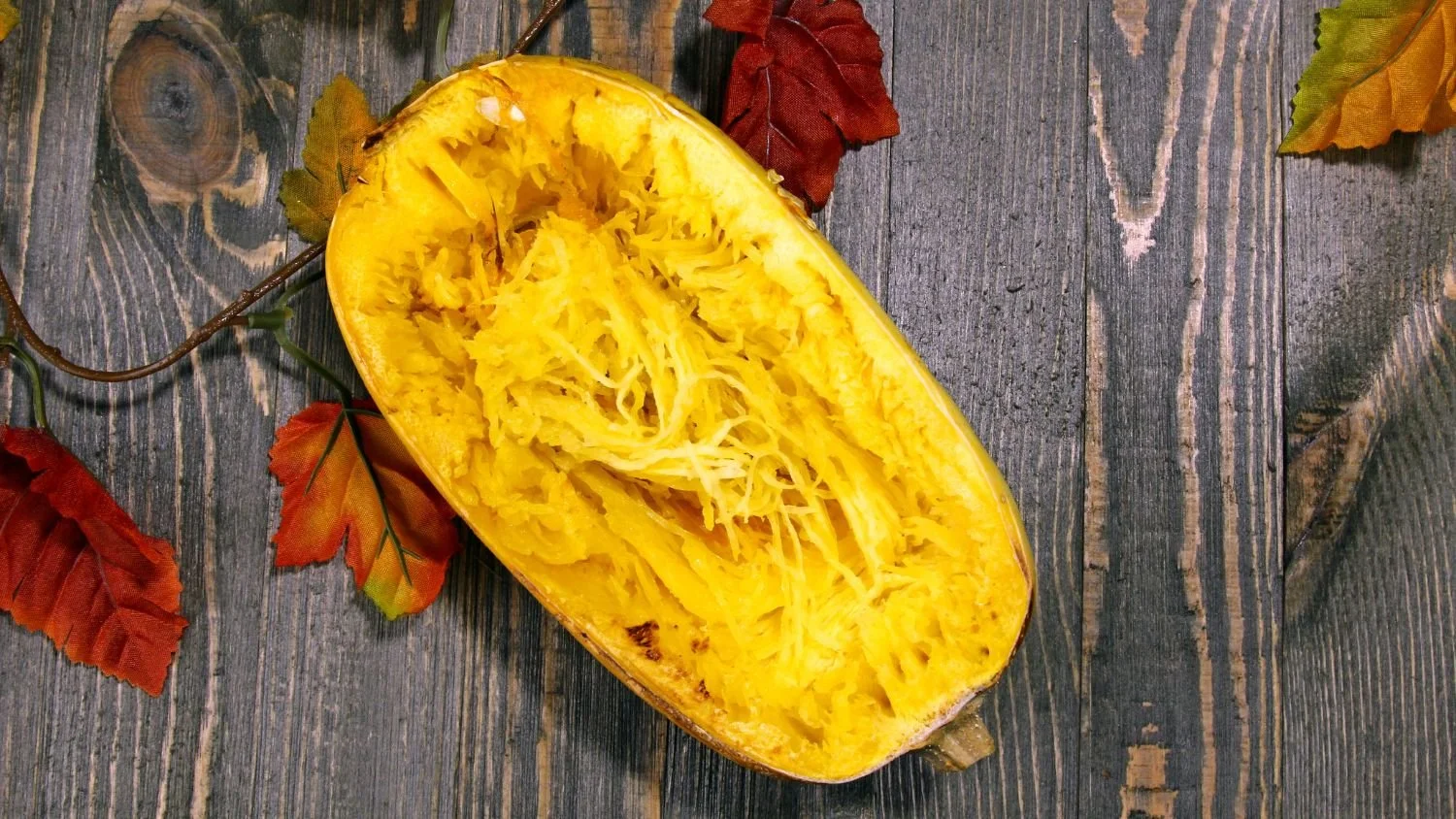 spaghetti squash half on a wood table with fall leaves
