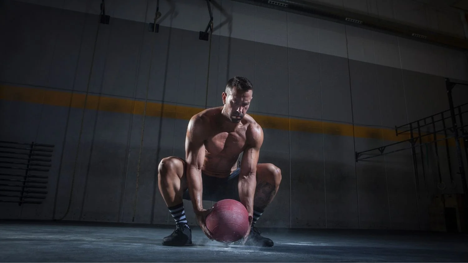 man in a squat position picking up a medicine ball in a dark room