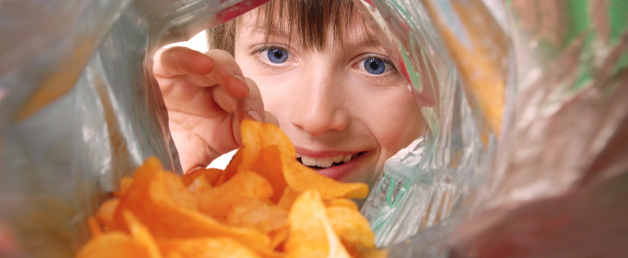 Photo of lady looking inside of the potato chips bag, reaching in for a chip. Shot from the inside of the bag perspective