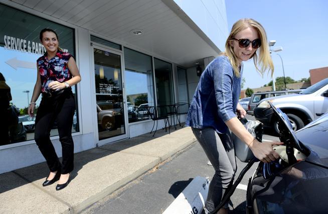 Michelle Daigle pulls the charging cord on her Nissan Leaf as Sara Cashin, Boulder Nissan's finance manager, looks on. ( Paul Aiken / File photo )