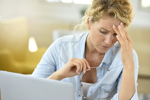 Woman sits at computer with hand on her forehead