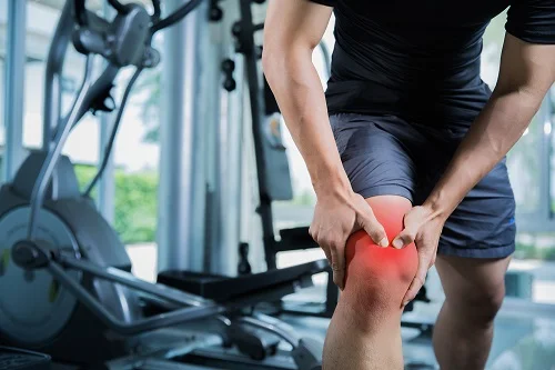 A man experiences knee pain at the gym
