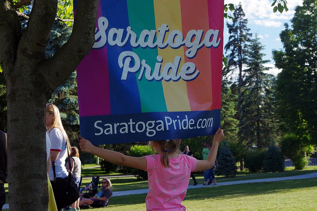 Sophie Smemo, 6, of Wilton, holds onto the Saratoga Pride sign hanging at Congress Park in downtown Saratoga during a vigil being held for the victims of the Pulse LGBTQ nightculb shooting in Orlando this past weekend, on Tuesday June 14, 2016 | PHOTO: Ryan Zidek
