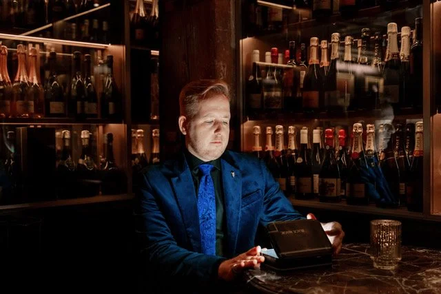 promo image James Alan at À Toi in Toronto surrounded by champagne bottles peering into a magic box
