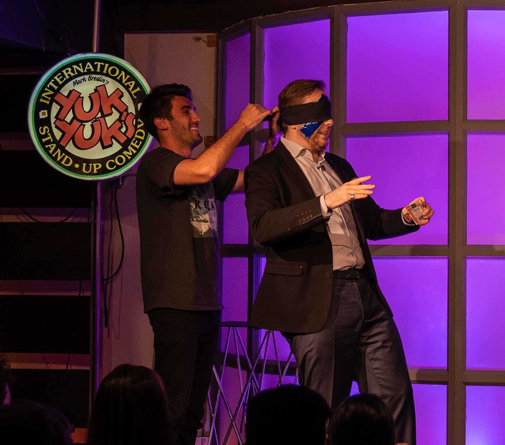 James Alan being blindfolded by audience member on stage at YukYuks in Toronto