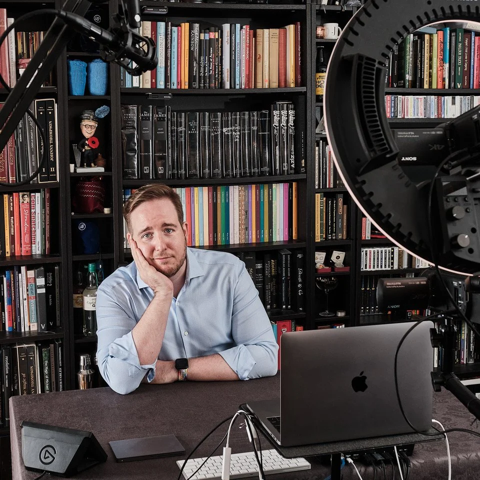 James Alan promo image posed with chin on hand in his Toronto virtual magic studio with wall of books