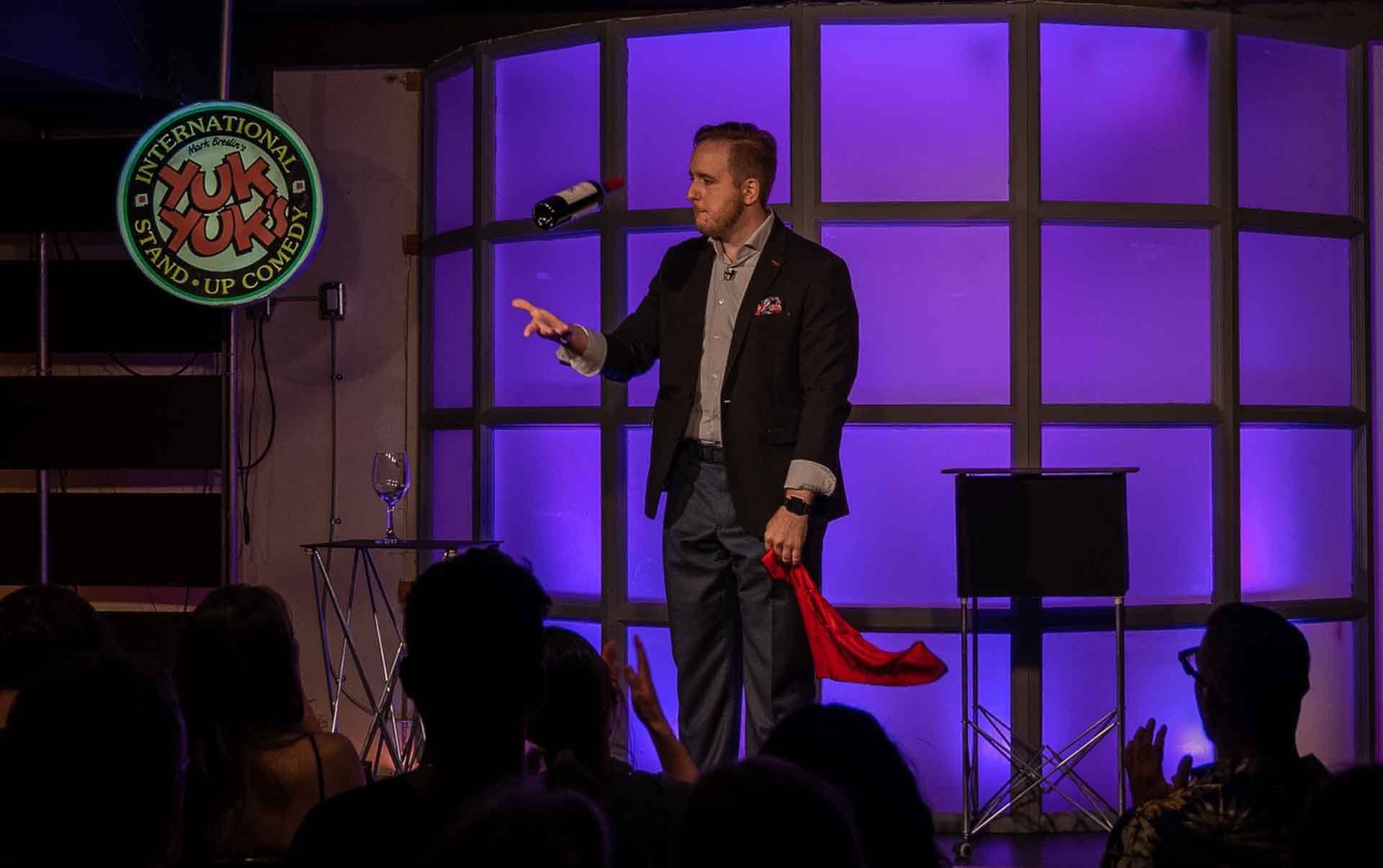 James Alan with a floating wine bottle on stage at YukYuks in Toronto