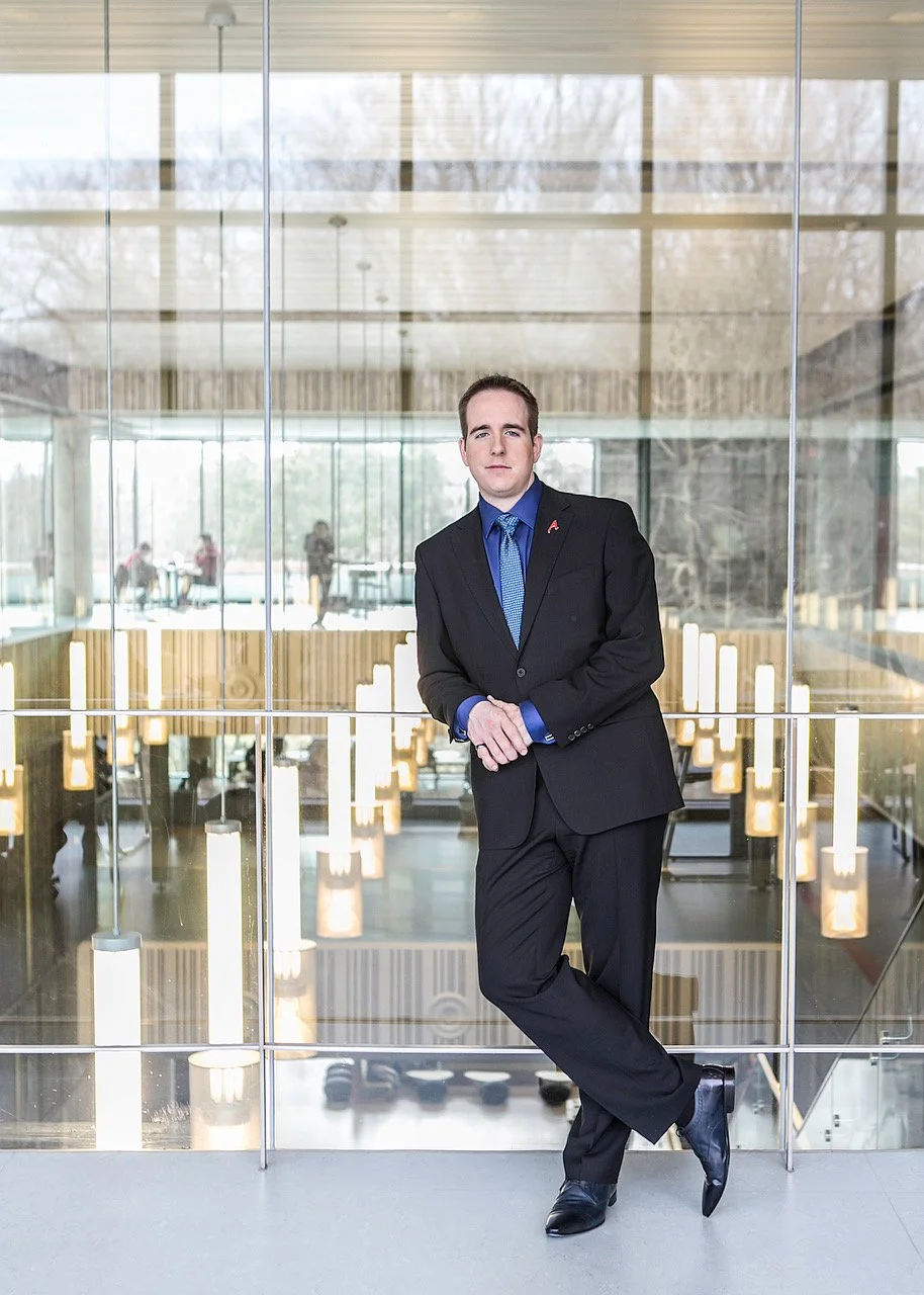 James Alan headshot in front of glass wall looking in on meeting rooms University of Toronto Mississauga Campus