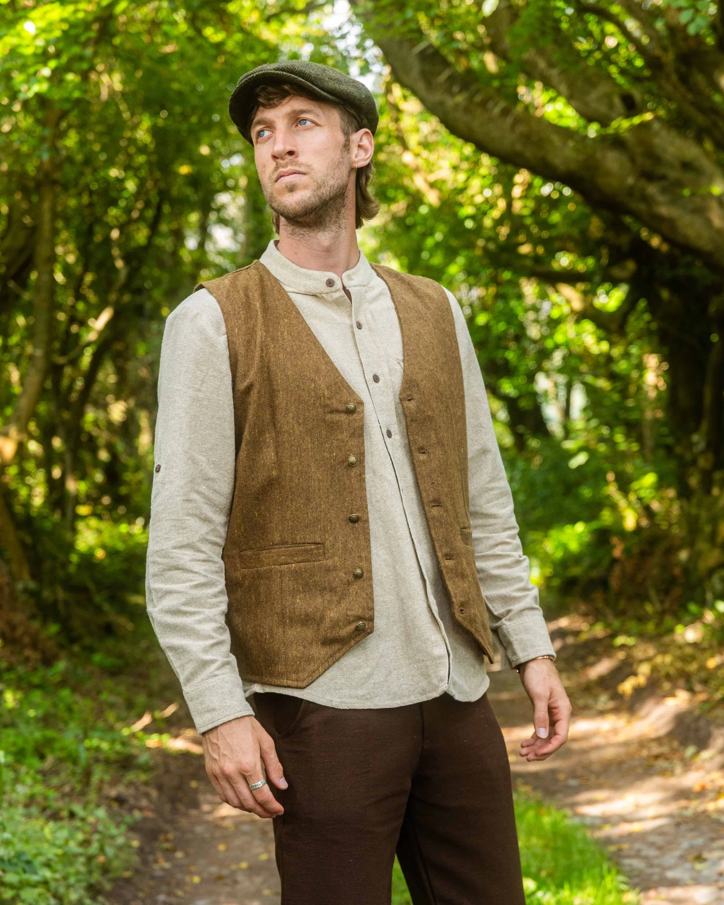 Man wearing a moss tweed Celtic vest standing in a forest and beside a tower ruin, showcasing front, back, and side details including antique-style buttons and adjustable back strap.