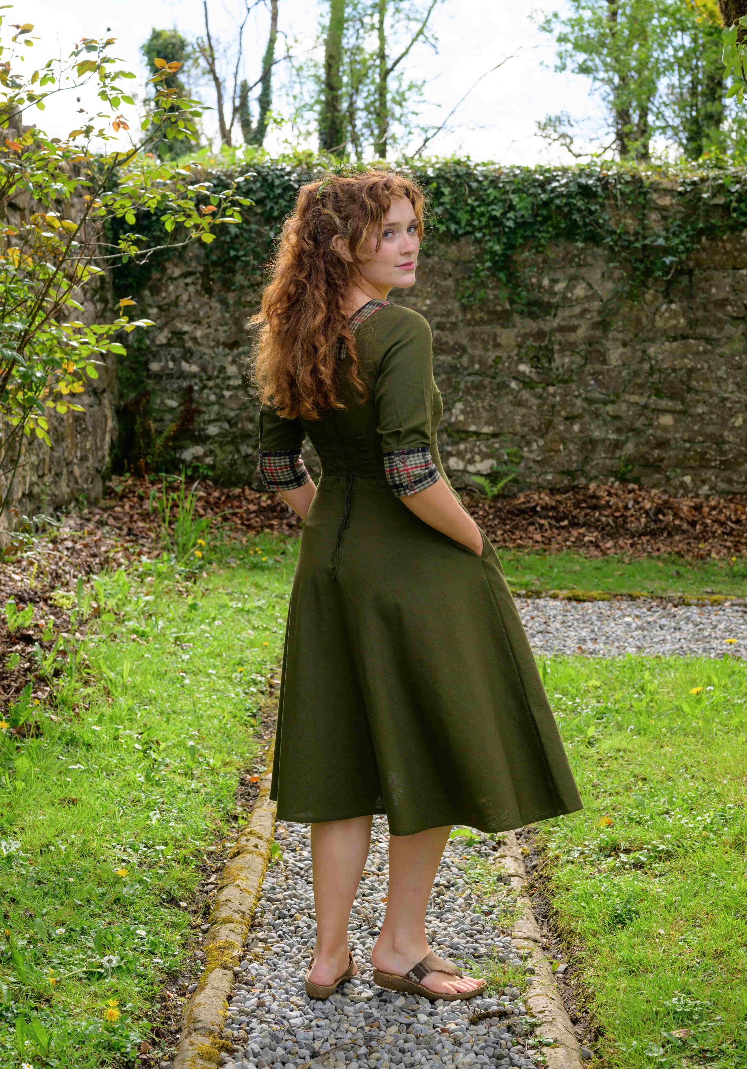 Discover our Olive Green Corset Midi Dress with pockets! This Irish design features a unique tweed detail, wide collar, and flowing skirt. The perfect cottagecore dream dress.