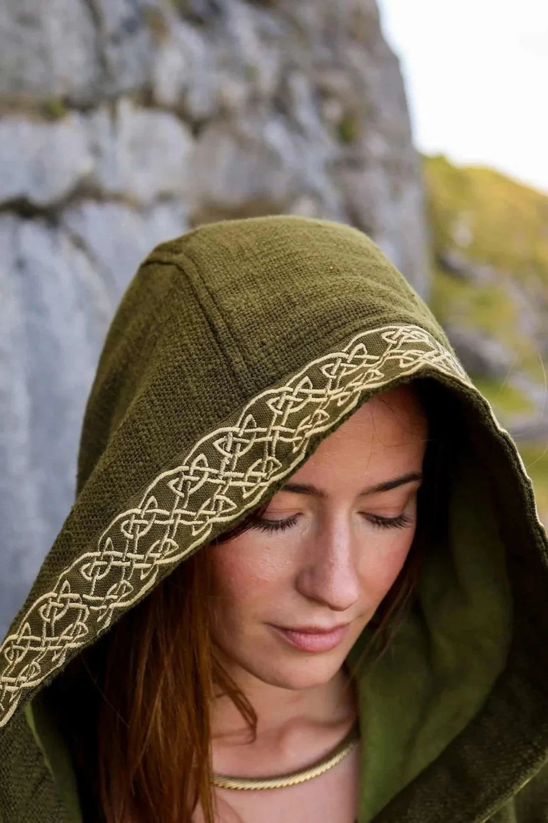 A woman wears the moss green Hooded Jacket with Fleece Lining and Embroidered Celtic Knotwork